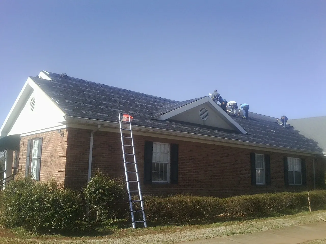 Crew tearing shingles off a brick ranch roof with a ladder set — Emergency Roof Repair work by our crew in Valley Village