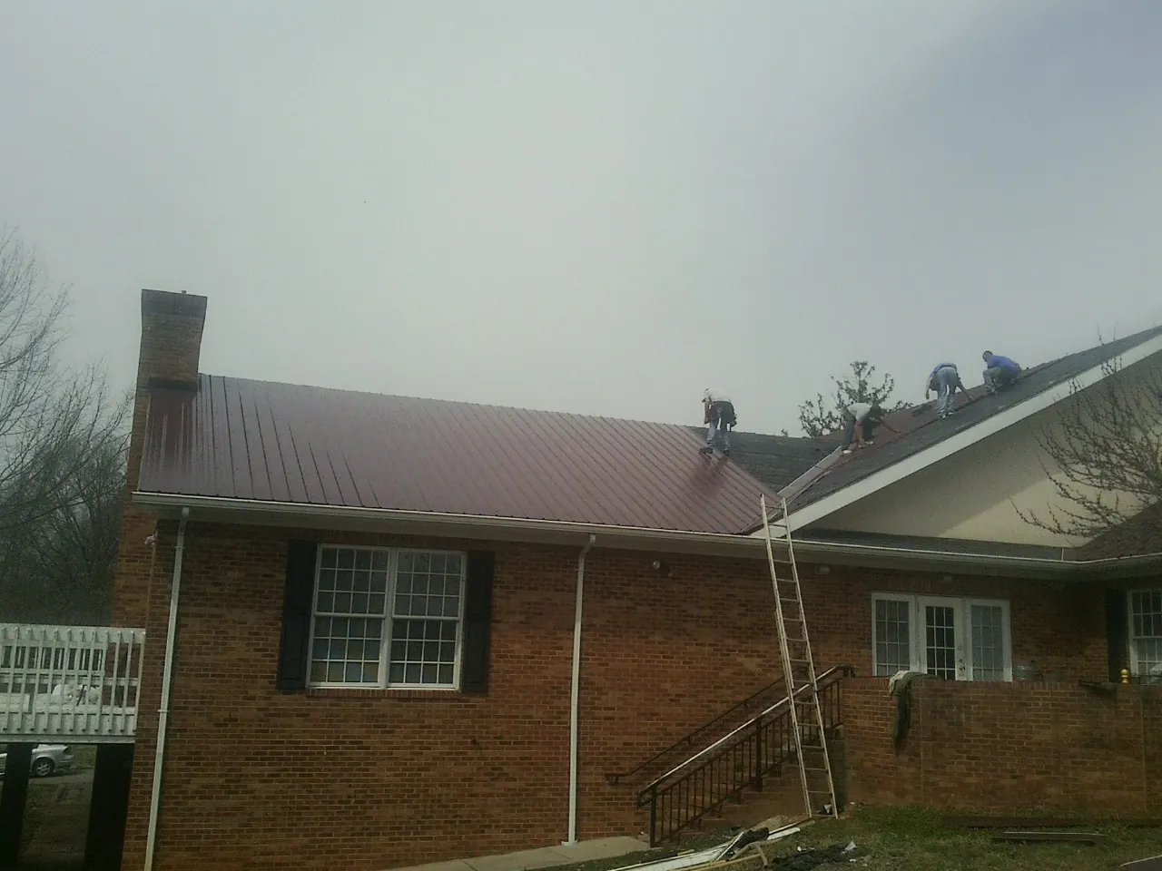 Crew setting red metal roofing panels on a brick home in Valley Village