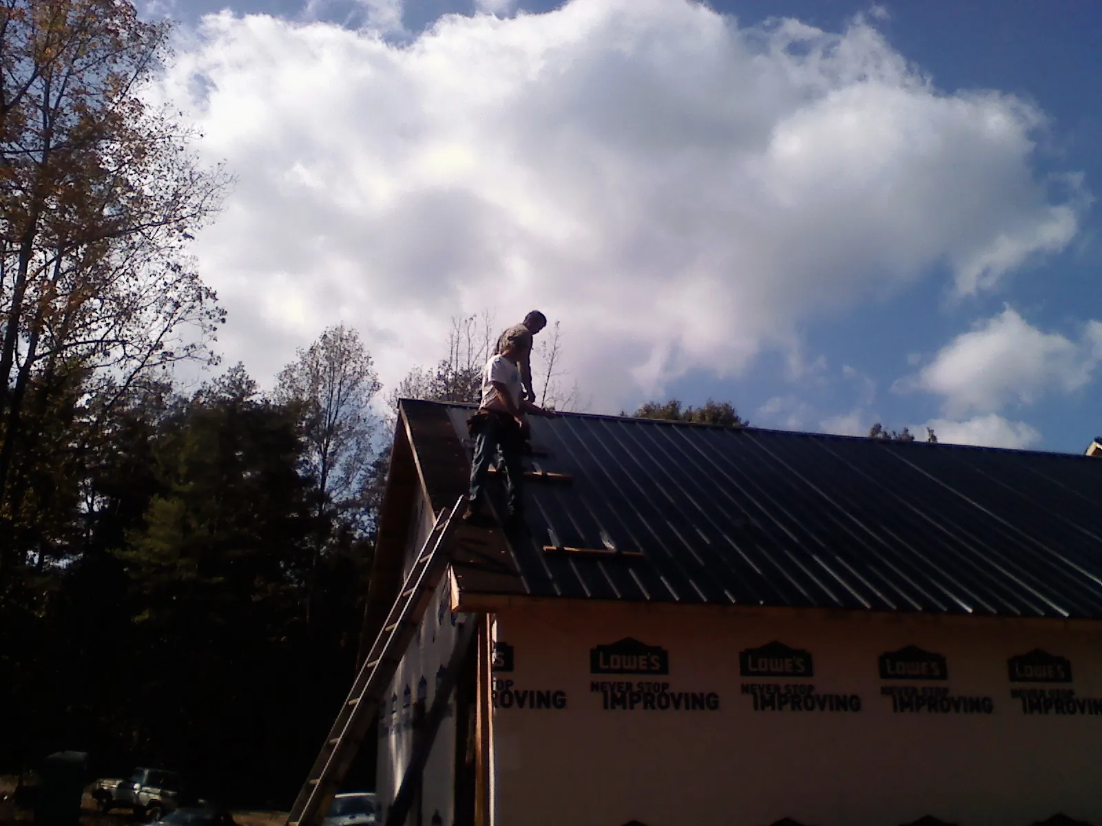 Roofer fastening dark metal panels high against a cloudy sky, from a Roof Inspection job in Valley Village