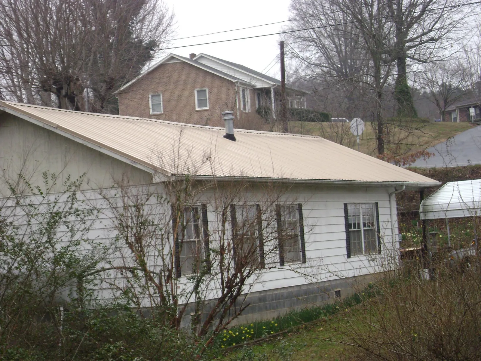 Tan metal roof on a white sided house set into a hillside — Commercial Roofing by Roofing Brothers in Valley Village